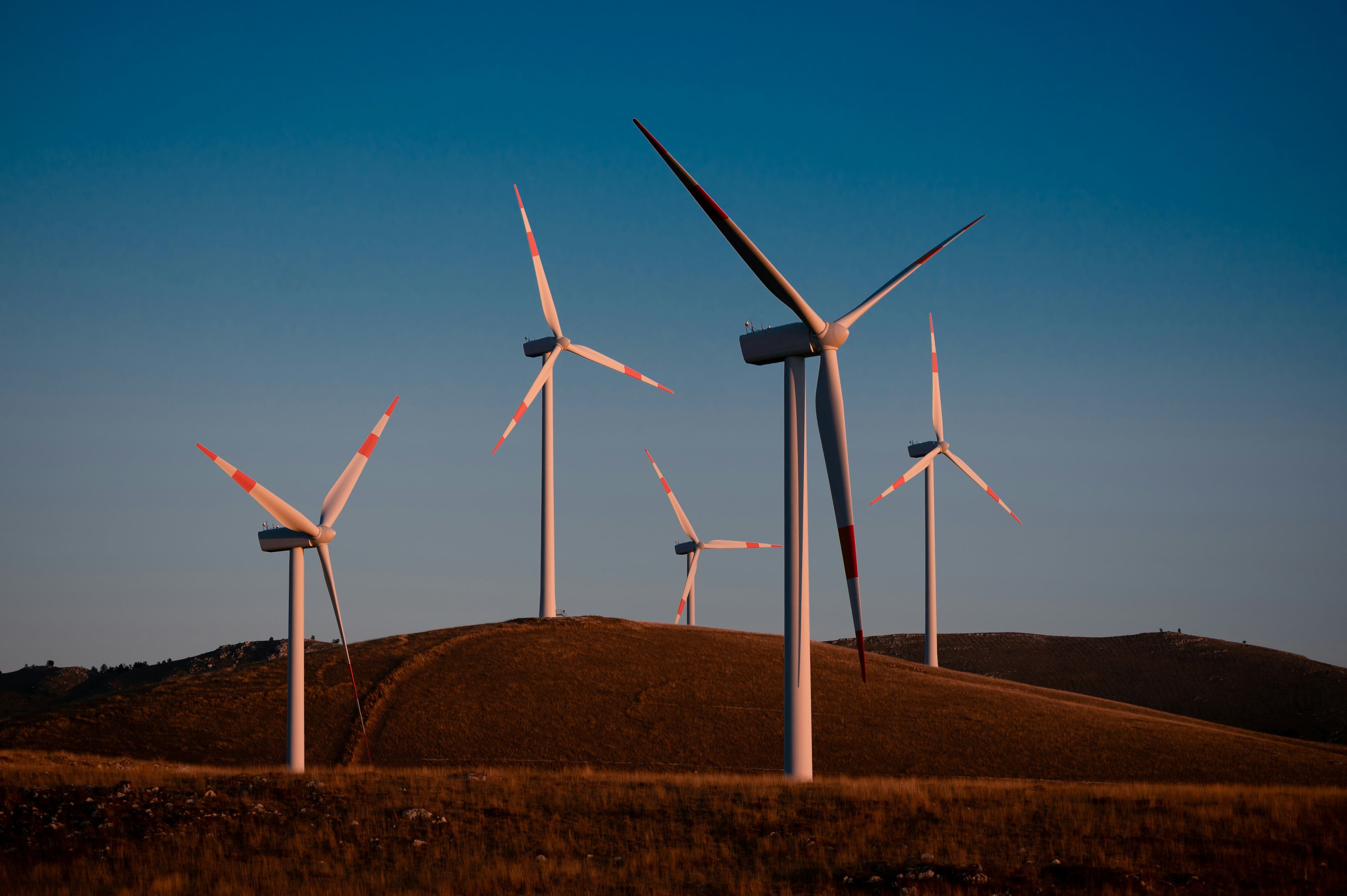 Wind turbines on a grassy hill under a clear blue sky, generating renewable energy.