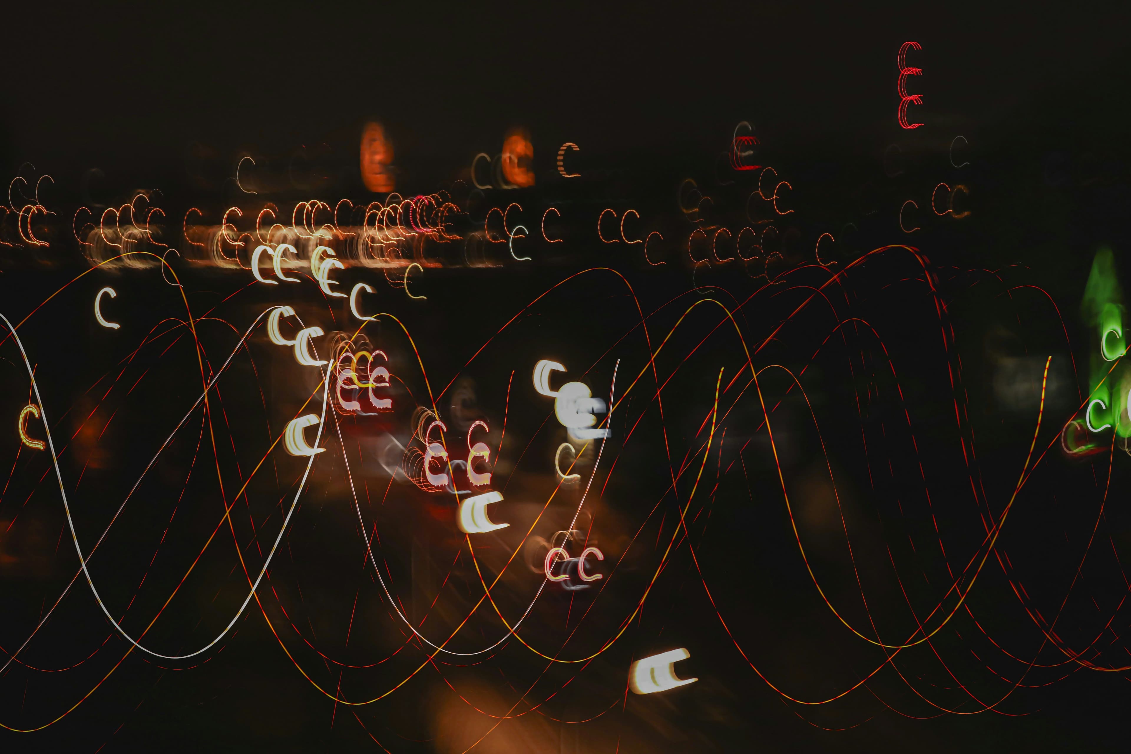 Abstract light trails in various colors create swirling patterns against a dark background, resembling a dynamic, chaotic night scene.